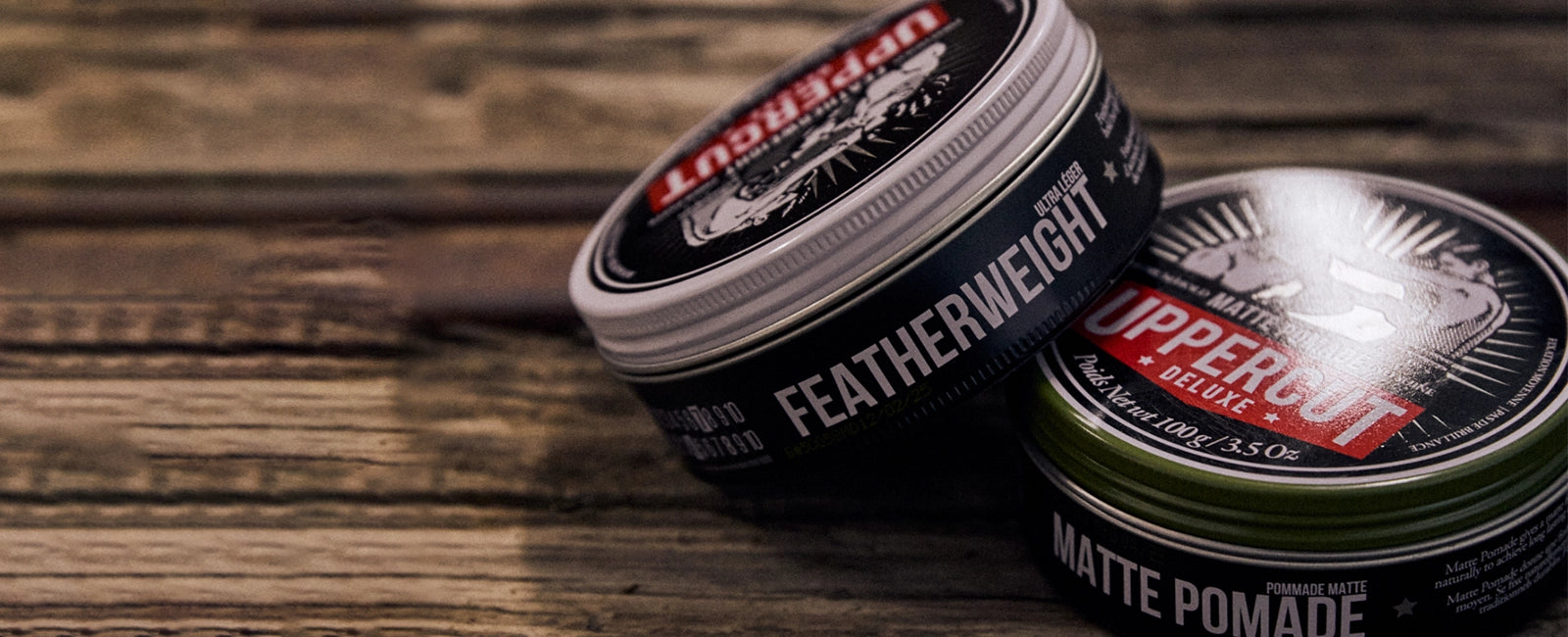 Two tins of Uppercut Deluxe pomade on a wooden surface