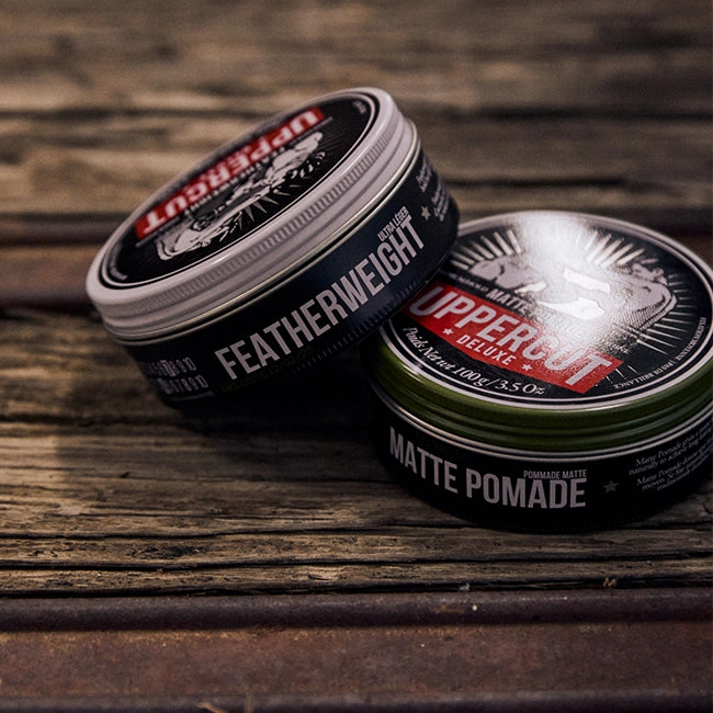Two tins of Uppercut Deluxe pomade on a wooden surface